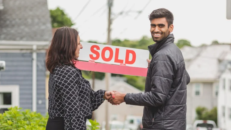 Two people shaking hands in front of a home while holding a “SOLD” sign, illustrating a successful sale for a Real Estate Selling Guide.