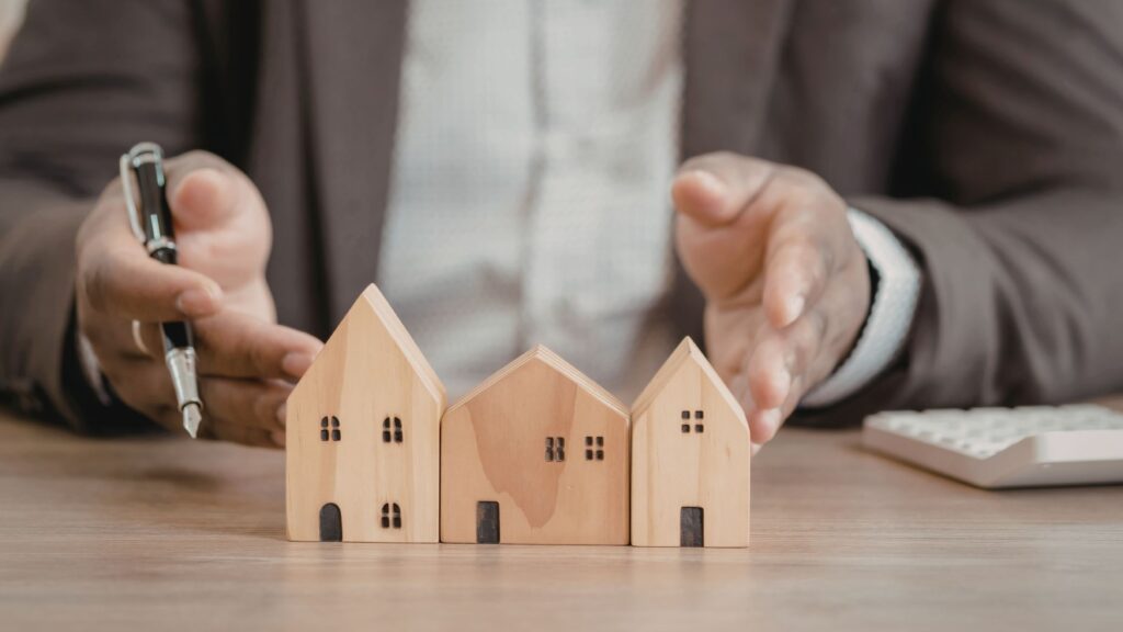 Desk with wooden house figures used to explain the challenges of self‑representation in real estate.