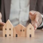 Desk with wooden house figures used to explain the challenges of self‑representation in real estate.