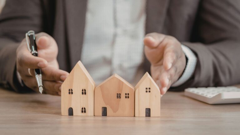 Desk with wooden house figures used to explain the challenges of self‑representation in real estate.